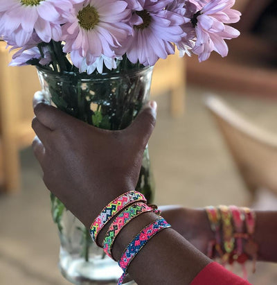 A model holding flowers and wearing the Electric Bali Friendship Bracelet Bundle from Love Is Project