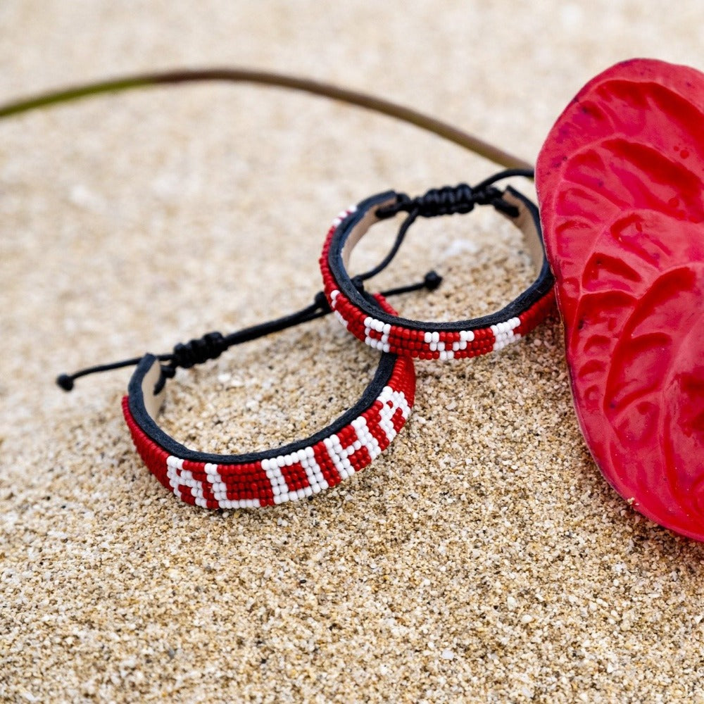 An Aloha Bracelet from Love Is Project in the sand next to a red flower
