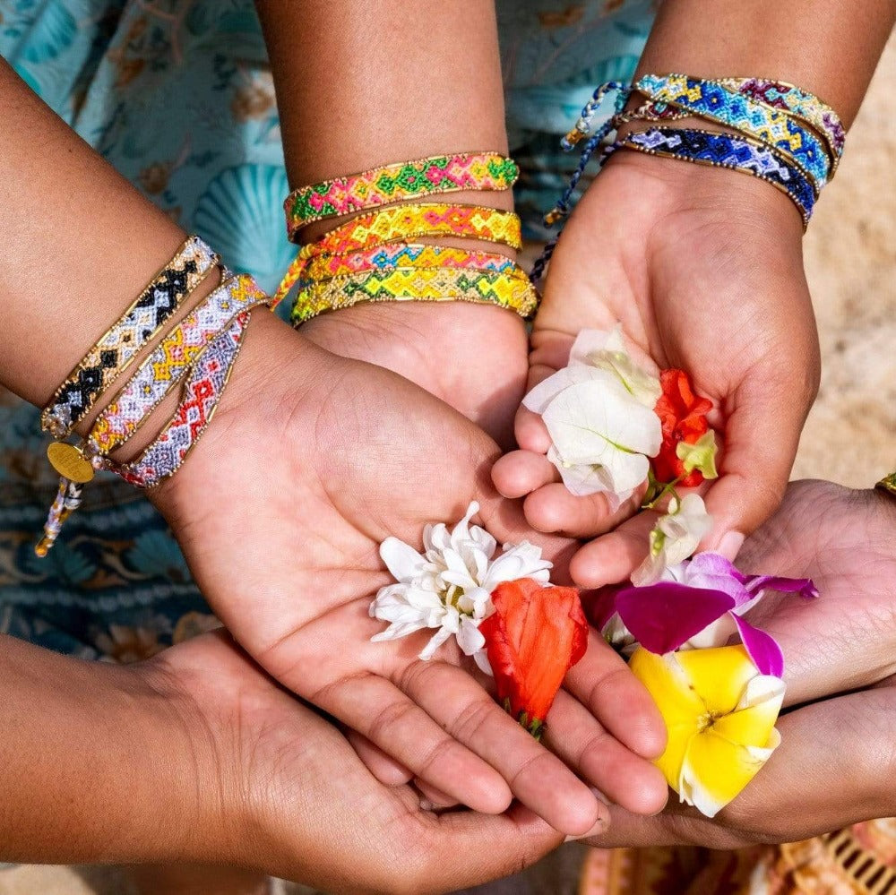A group of models holding flowers and wearing the Quartz Bali Friendship Bracelet Bundle from Love Is Project