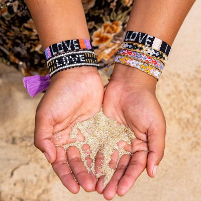 A model holding sand and wearing the Quartz Bali Friendship Bracelet Bundle from Love Is Project