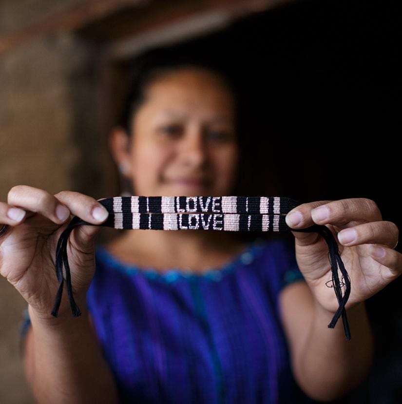 An artisan holding up the Black and Neutral Atitlan LOVE Bracelet from Love Is Project