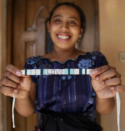 An artisan holding a Green and White Atitlan LOVE Bracelet from Love Is Project
