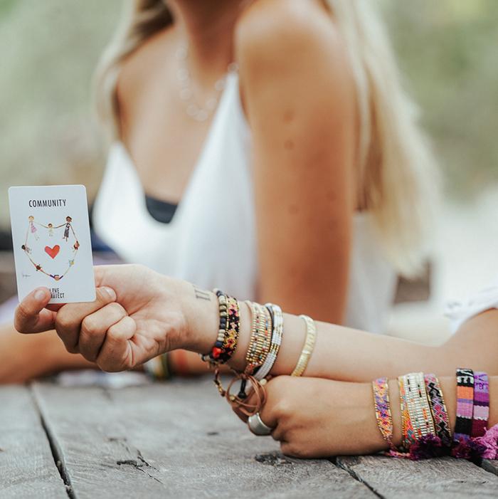 A model wearing the Galaxy Bali Friendship Bracelet Bundle from Love Is Project and holding the Spread the Love Deck of Cards